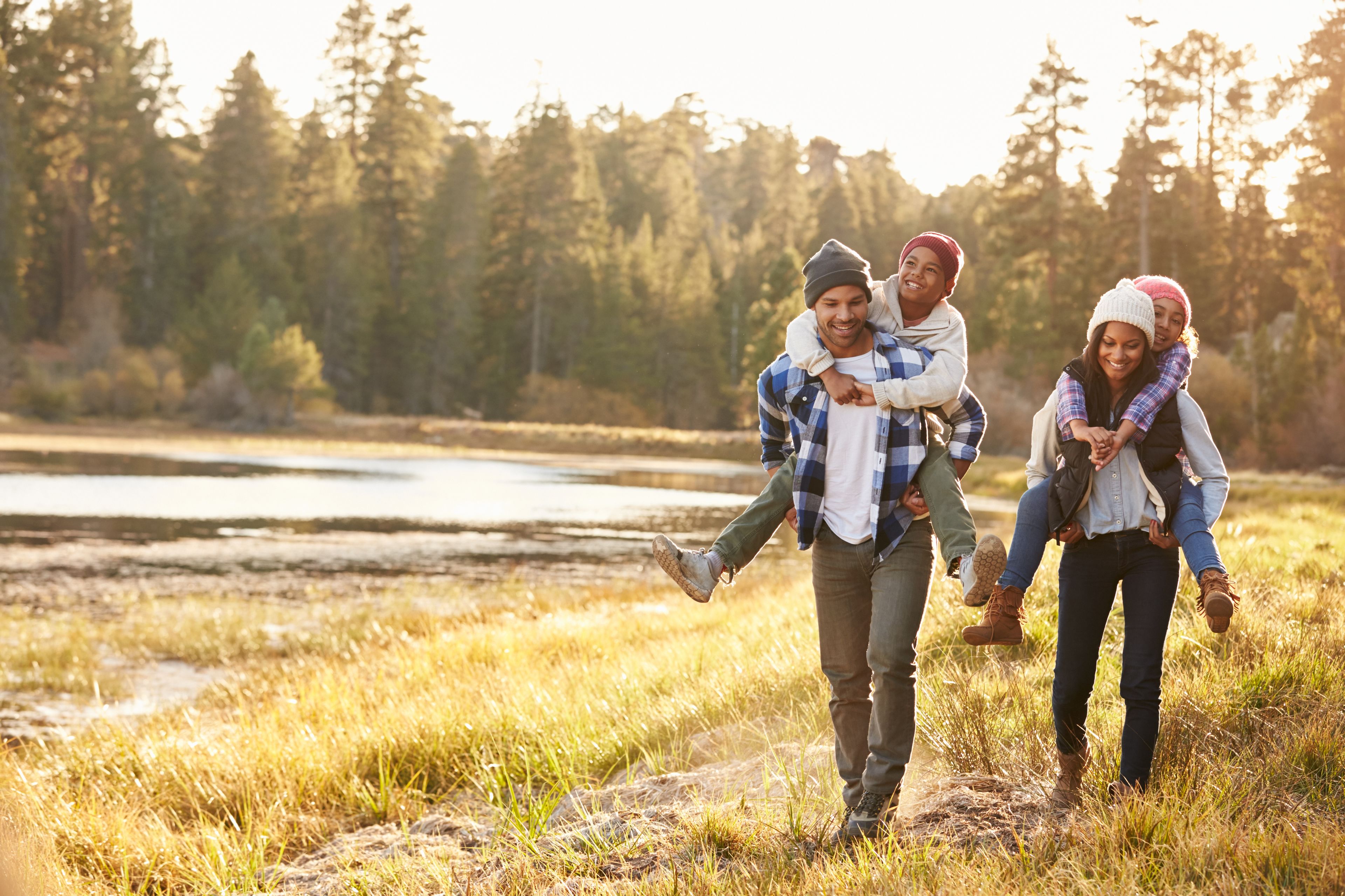 Una familia caminando por un campo con césped, un lago y árboles al fondo.