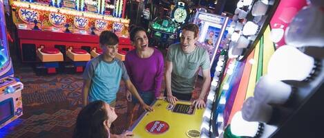 A group of people playing a slot machine game in an arcade with colorful machines and a patterned carpet.