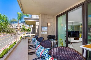 A balcony with wicker chairs, a grill, and a TV in a modern room. - Surfside Life (Oceanside)