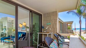A modern living area with a sofa, chairs, and a table, overlooking a beach and a building. - Surfside Life (Oceanside)
