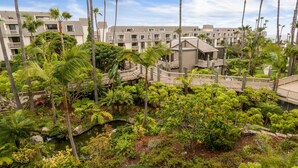 A resort with multiple-story buildings, palm trees, and a well-maintained garden with a small water feature. - Paradise Found (Oceanside)
