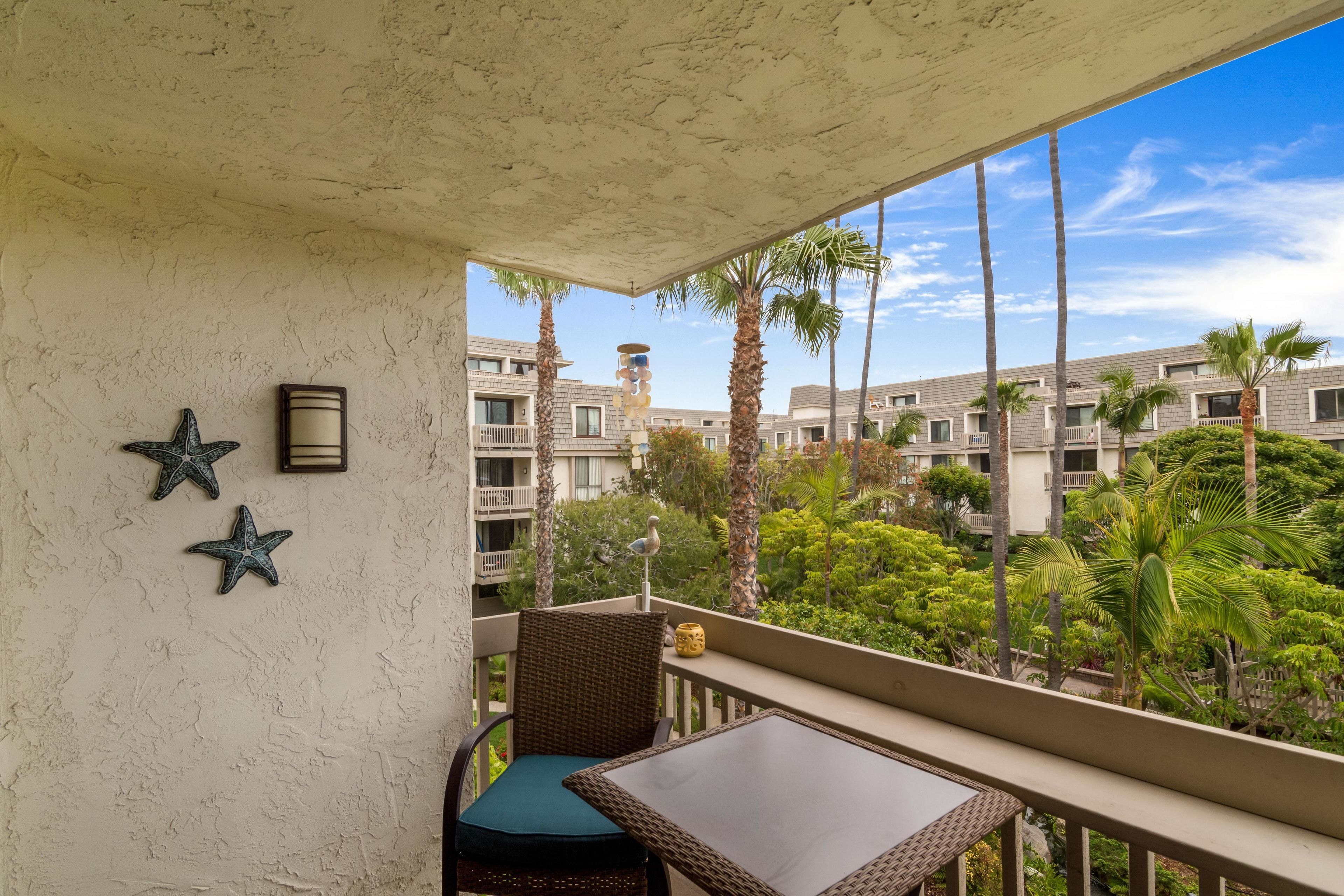 Un balcón con mobiliario de mimbre, decoraciones con estrellas y vistas a palmeras y edificios.