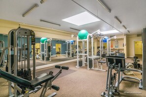 A gym with various exercise machines, mirrors, and a ceiling fan. - Paradise Found (Oceanside)