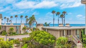 A coastal hotel with multiple-story buildings, palm trees, and a view of the ocean. - Ocean Breeze Retreat (Oceanside)