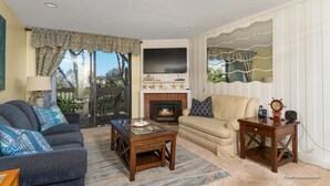 A living room with a fireplace, a sofa, a coffee table, and a television. - Starfish Cove (Oceanside)