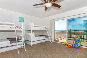A room with two bunk beds, a ceiling fan, a window with a view of the ocean, and a slide set up outside. - Seaside Villa (Oceanside)
