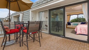 A balcony with a table and chairs, a sliding glass door leading to a bedroom, and a large umbrella. - North Coast Village G-306 Blue Horizons (Oceanside)