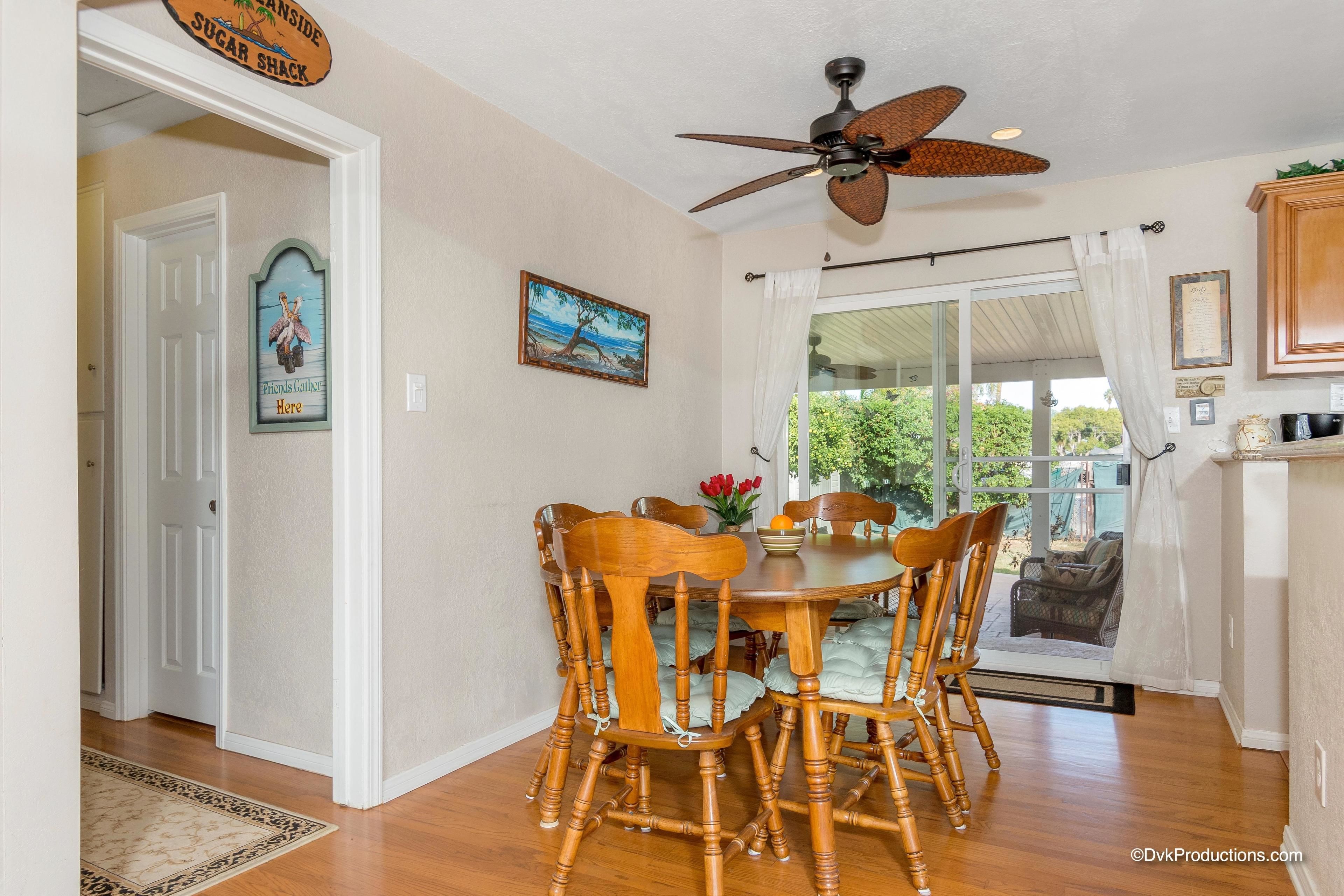 A dining area with a round table, wooden chairs, a ceiling fan, and a view of the outdoors through a glass door.