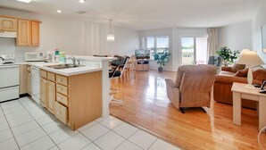 A modern apartment with a kitchen, dining area, and living room. It includes wooden cabinets, a white countertop, a dining table, and a sofa. - Amadeus 7-Close to it all, Private Balcony, Pool! (Treasure Island)