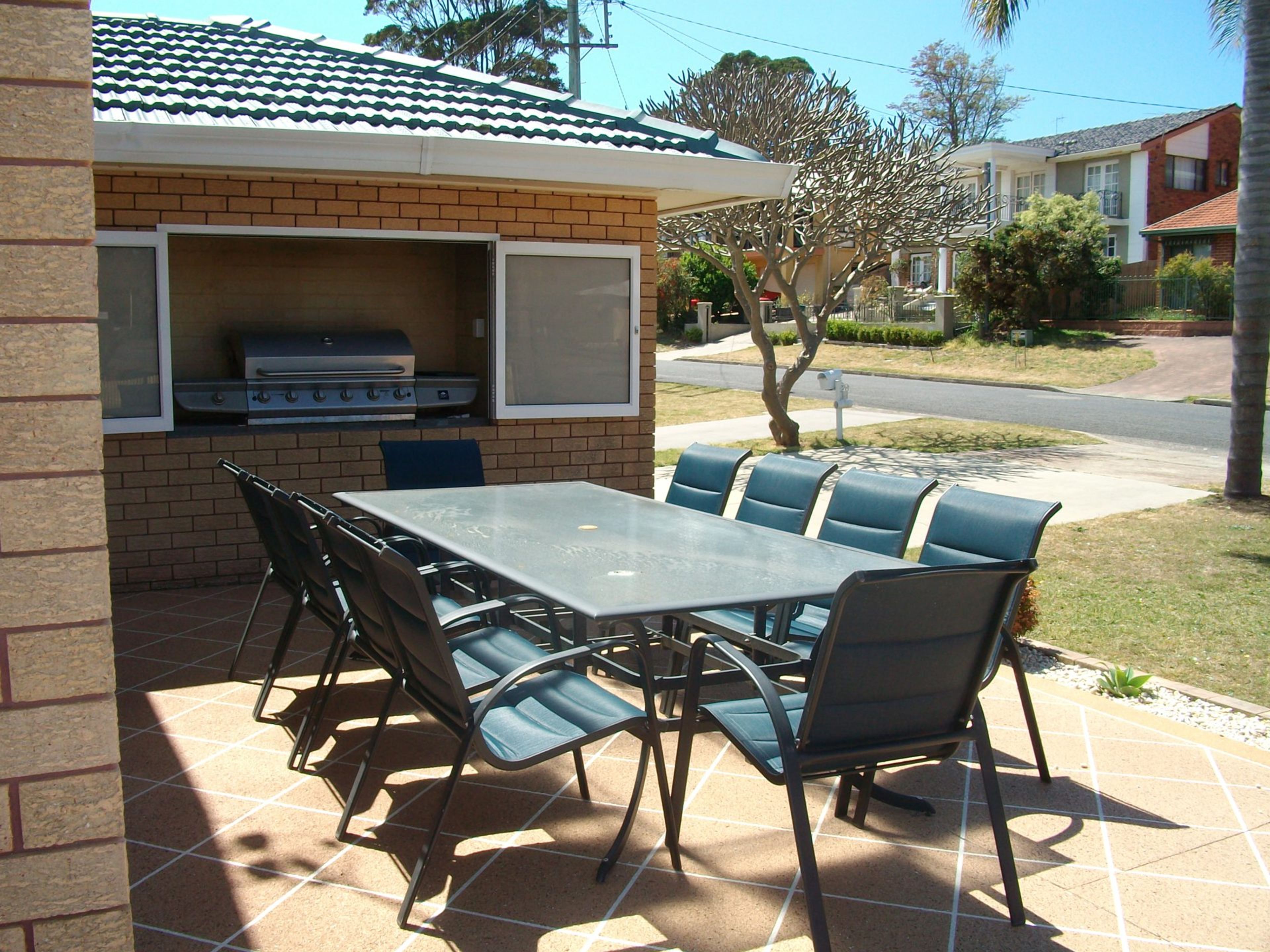 An outdoor patio with a brick barbecue area, a table, and chairs.