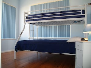 Een stapelbed met een ladder, een nachtkastje met een lamp en een raam met zonwering.