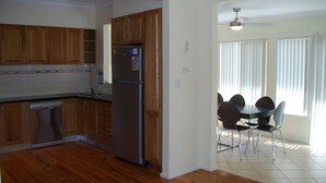 Una cocina con armarios de madera, un refrigerador de acero inoxidable y un lavavajillas. Hay un comedor con una mesa y sillas.