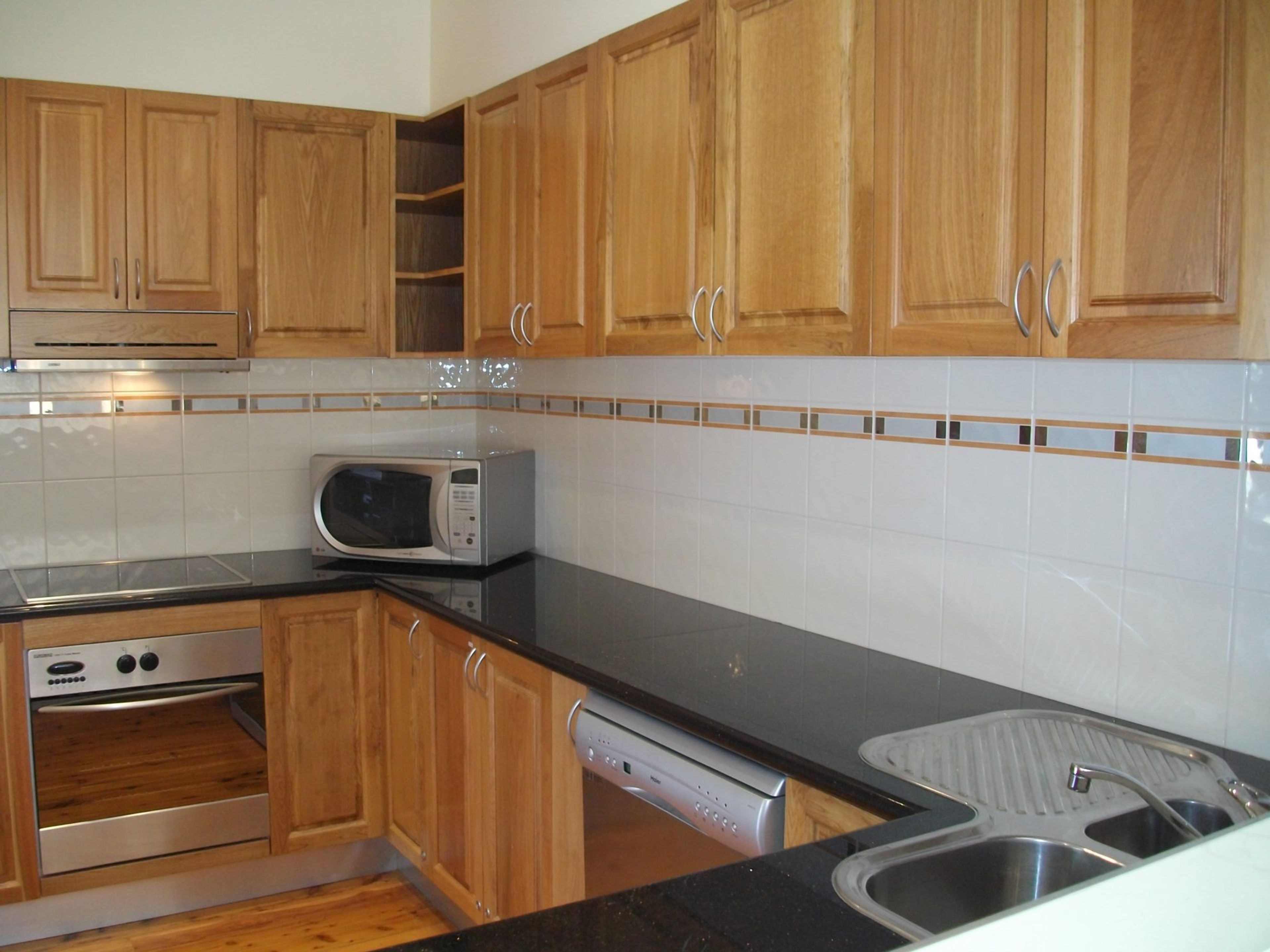 A kitchen with wooden cabinets, a microwave, a dishwasher, and a stainless steel sink.