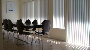 Un comedor con una mesa redonda y sillas, ventanas amplias con persianas y piso de baldosas.