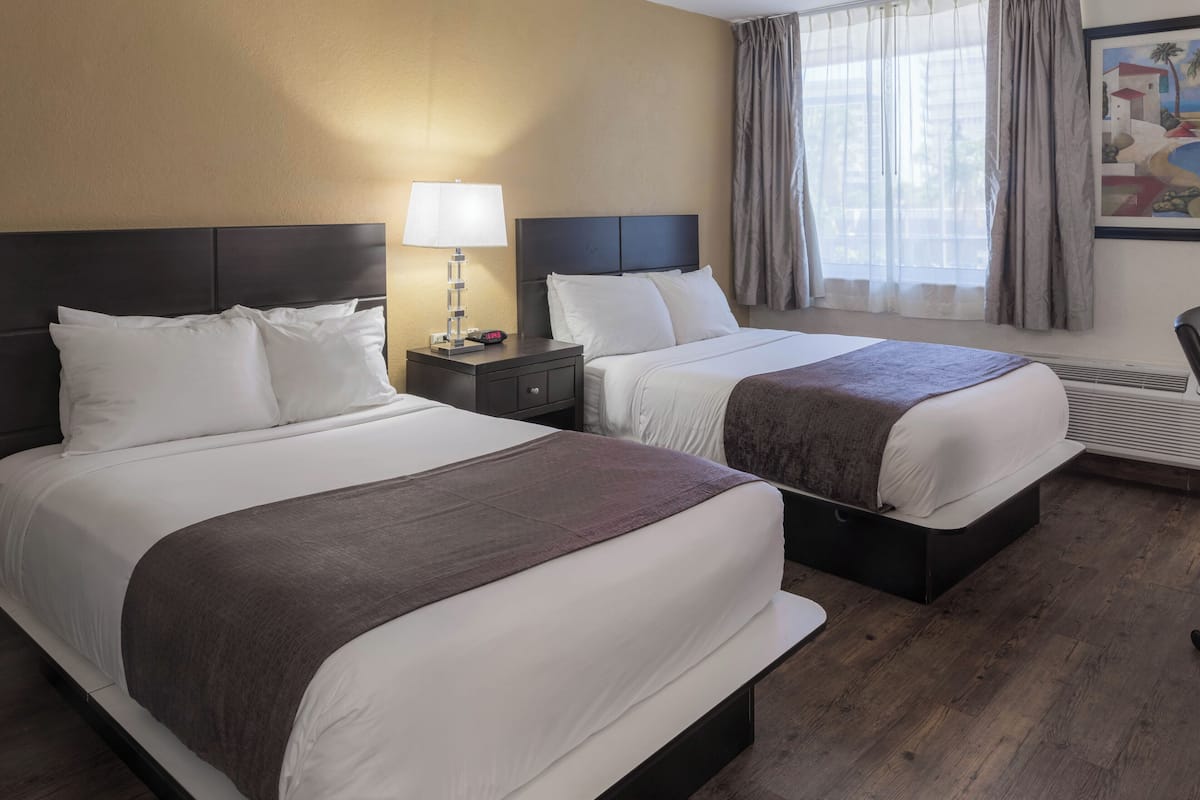 A hotel room with two beds, a nightstand with a lamp, a painting on the wall, and a window with curtains.