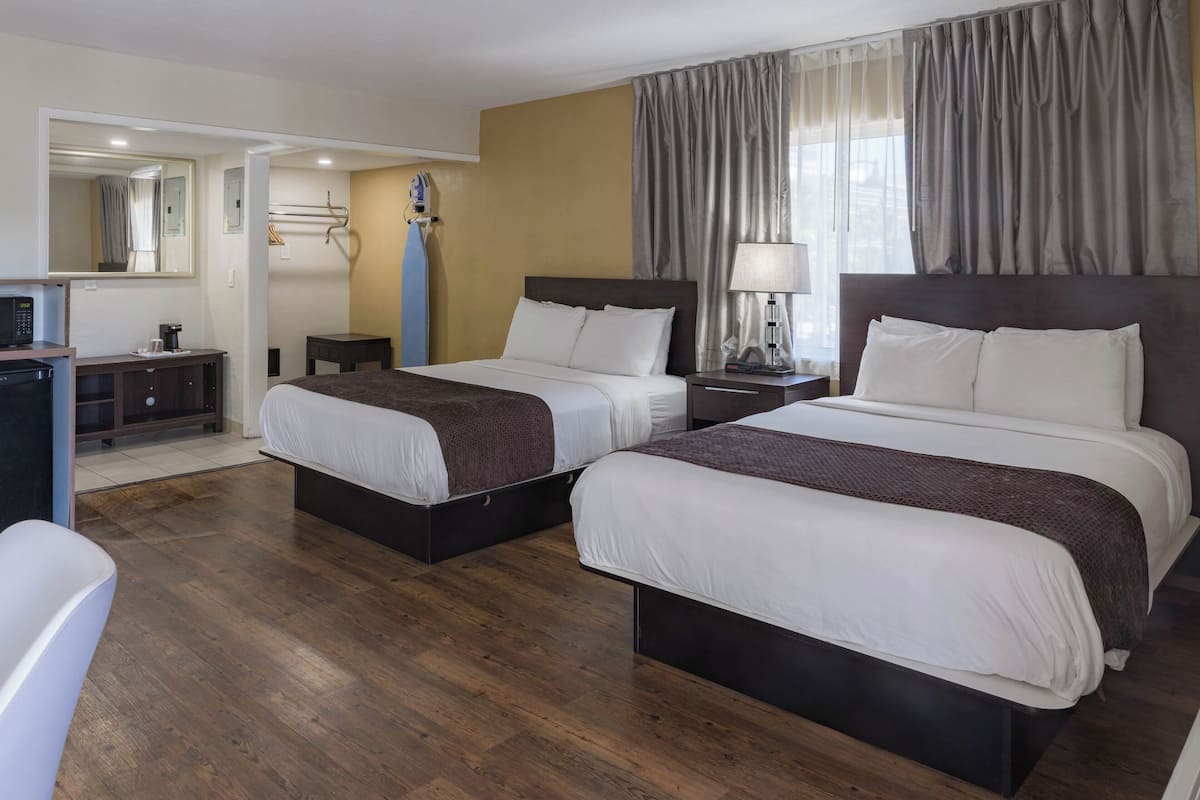 A hotel room with two beds, a desk with a computer, a mirror, and a window with curtains.