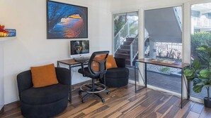 Un espacio de oficina moderno con un escritorio, dos sillas negras con cojines anaranjados, una computadora y un amplio ventanal con vistas a una escalera y zona exterior.