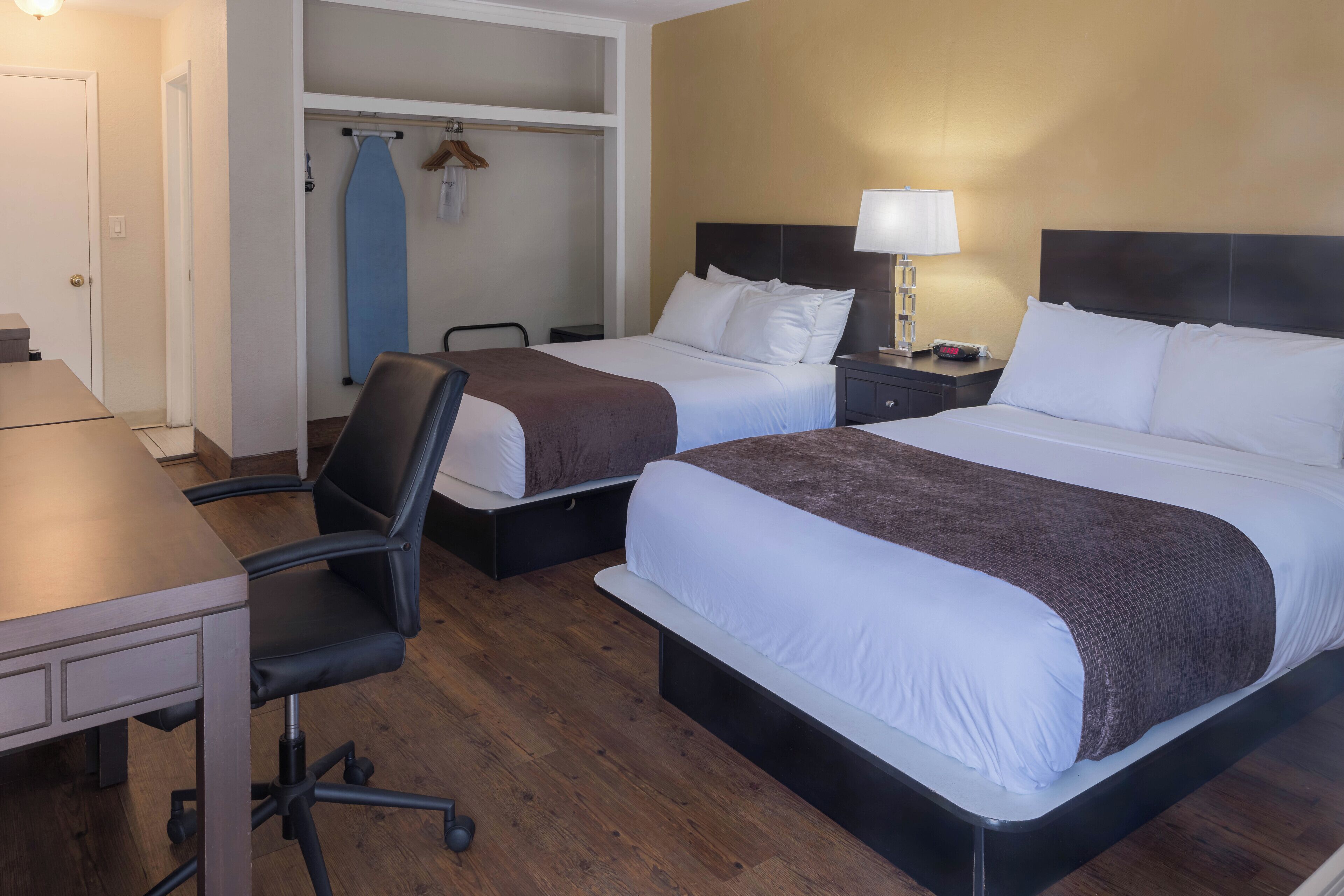 A hotel room with two beds, a desk, and a chair.