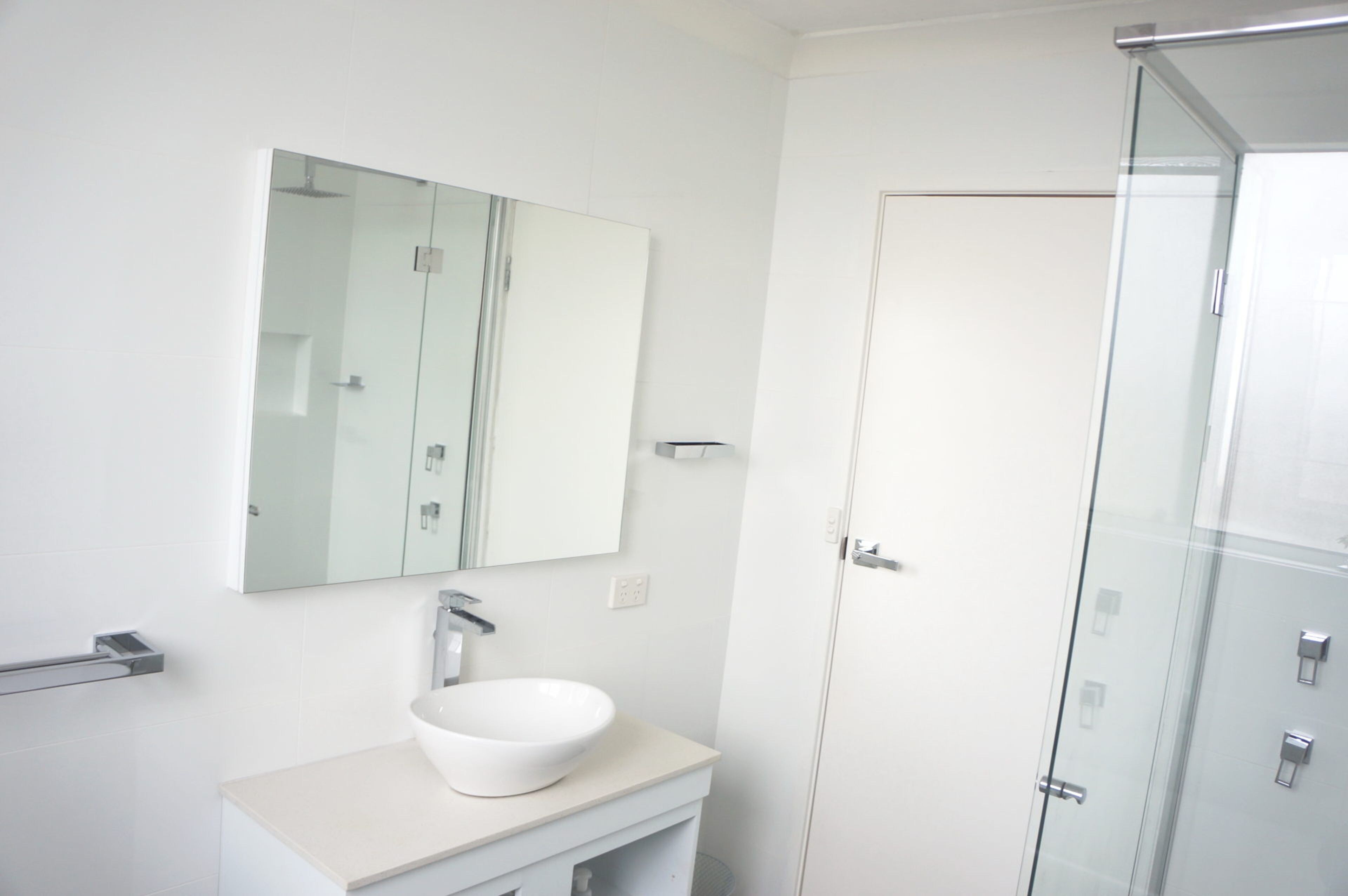 A bathroom with a white sink, a mirror, and a glass shower enclosure.