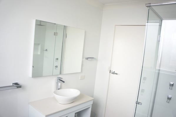 A bathroom with a white sink, a mirror, and a glass shower enclosure.
