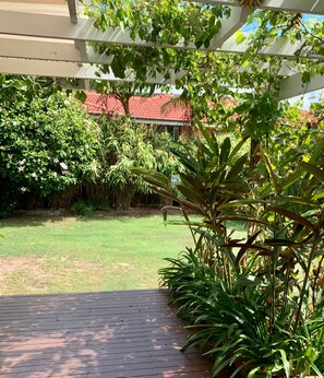 A covered patio area with a view of a red-roofed building and various green plants.
