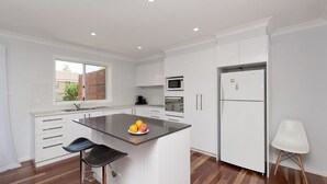 A modern kitchen with white cabinets, a central island with fruit, a microwave, and a refrigerator. - Eden by the Bay, 98 Sandy Point Rd - Large family home just 300m to Corlette Beach (Corlette)