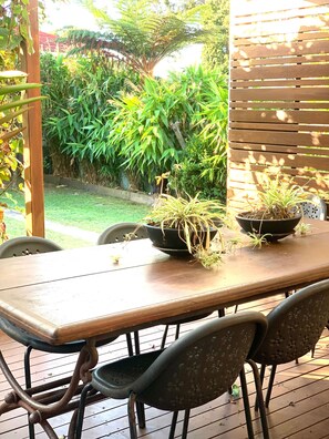 Een houten tafel met stoelen, bloempotten en een houten omheining in een tuin.