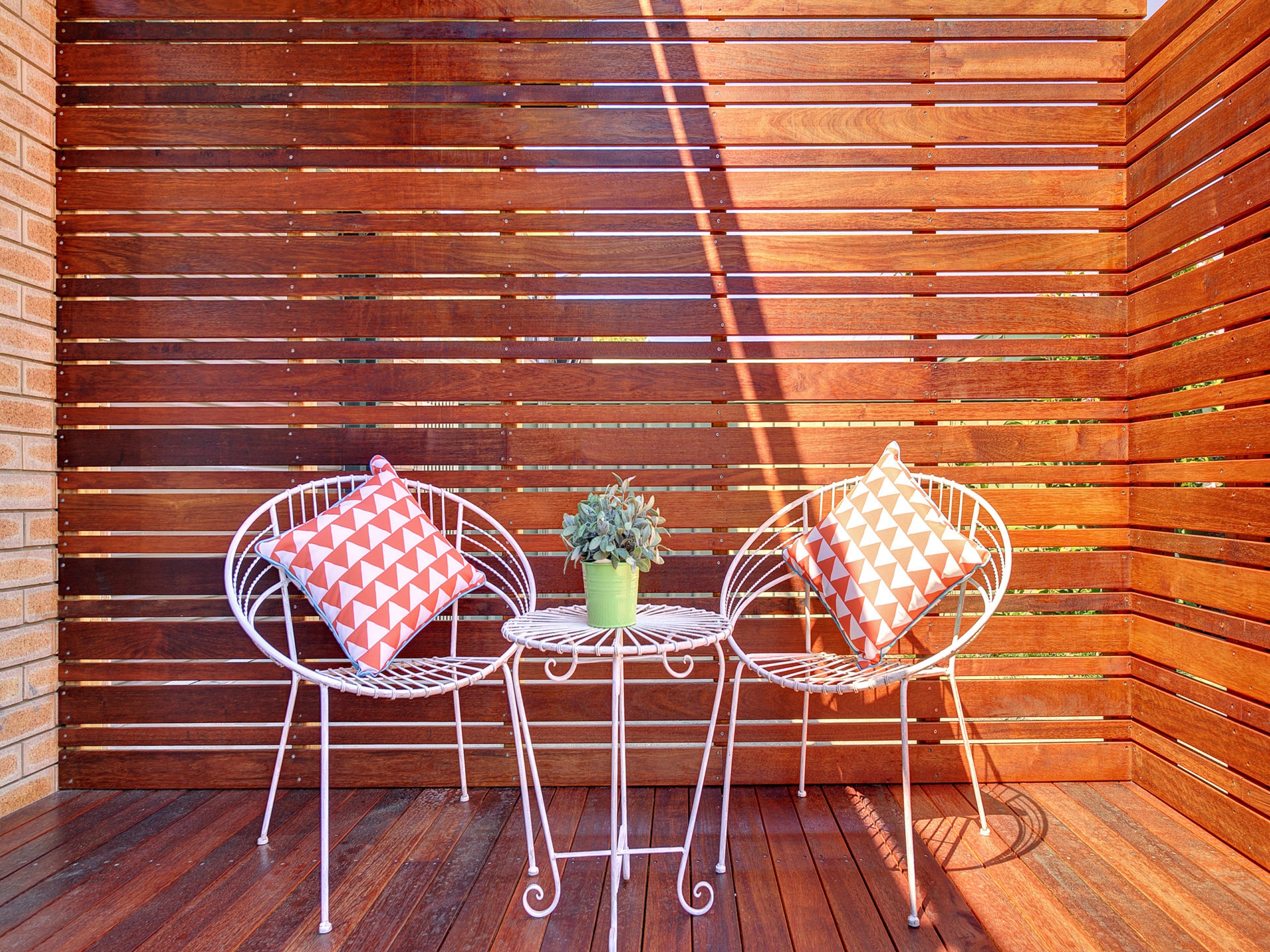 A wooden deck with two white metal chairs and a small table, each with a patterned cushion.