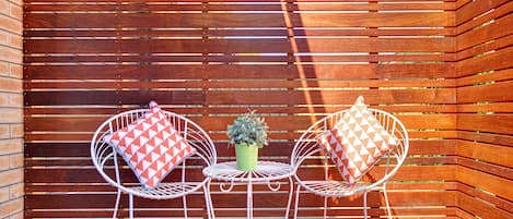 A wooden deck with two white metal chairs and a small table, each with a patterned cushion.