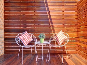 A wooden deck with two white metal chairs and a small table, each with a patterned cushion.
