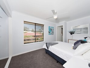 Een slaapkamer met een bed, een plafondventilator, een raam met uitzicht, een schilderij en een spiegel.