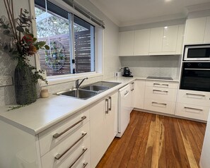 A modern kitchen with white cabinets, a stainless steel sink, and a built-in oven.