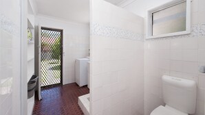 A bathroom with white tiles, a red patterned floor, a toilet, and a window. - Eden by the Bay Faimly Home near Corlette Beach (Corlette)