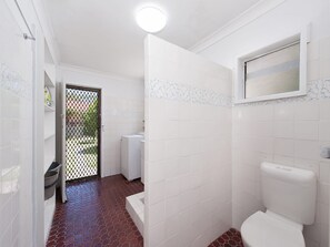 Een badkamer met witte tegels, een vloer met rood patroon, een toilet en een raam.
