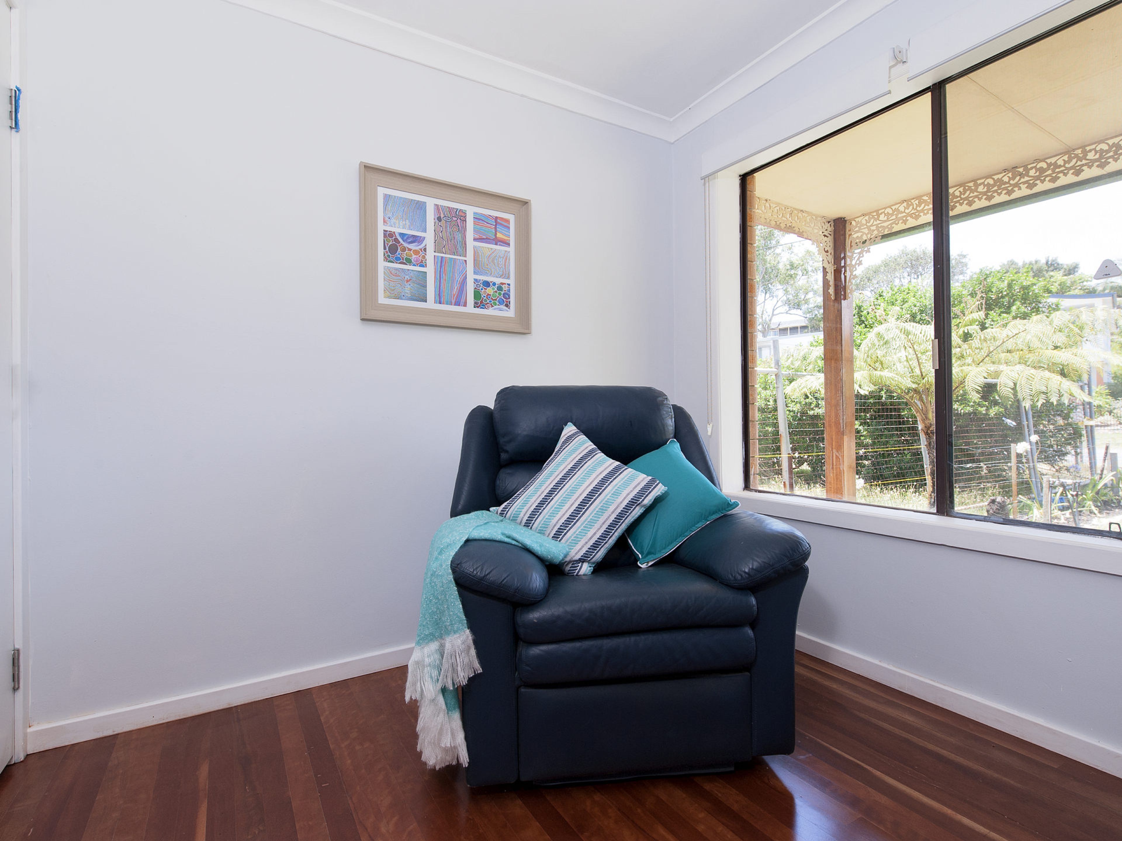 A room with a dark leather armchair, a teal throw blanket, and a framed abstract art piece on the wall.