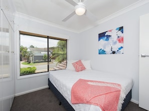 A bedroom with a bed, a window, a ceiling fan, and a wall with a painting.