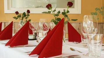 Una mesa de comedor con servilletas rojas, copas de vino transparentes y un jarrón con rosas rojas.