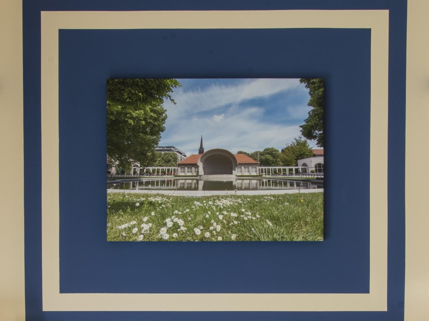 A square frame with a photograph of a building with a red roof and a spire, surrounded by greenery and a body of water.