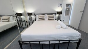 Ein Hotelzimmer mit einem Einzelbett, zwei Nachttischen mit Lampen, einem Spiegel und einem Kleiderschrank.