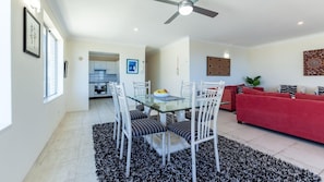 A modern living room with a glass dining table, white chairs, a red sofa, and a ceiling fan.