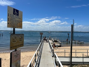 Een strand met een houten looppad naar het water, borden die duiken en springen verbieden, en een bord met een beschermd natuurgebied.