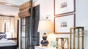 A bedroom with a bed, a white cabinet with glass doors, a door with a woven mat, and framed pictures on the wall.