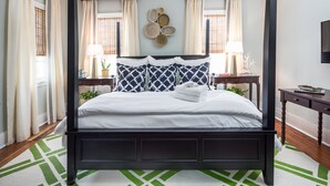 A four-poster bed with white bedding, two bedside tables with lamps, and a wall-mounted decorative piece.