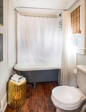 A bathroom with a bathtub, toilet, and a small wooden stool with toiletries.