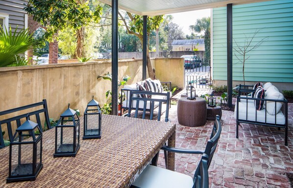 A covered patio with a wicker table and chairs, a small round table, and a bench.