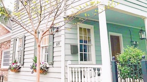 A two-story house with a green and white exterior, a white porch with a balustrade, and a tree with green leaves. - 69B Spring Street - 2 BR / 1 BA Holiday home 2 (Charleston)