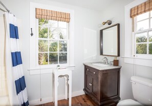 A bathroom with a window, white vanity, dark wooden cabinet, and a white toilet. - 71B Spring Street - 3 BR / 1.5 BA Holiday home 3 (Charleston)