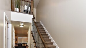 Eine Treppe mit Holzsitzen und einem Metallgeländer, die zu einer Empfangsebene im zweiten Stock mit einem Blumentopf und einem Stuhl führt.