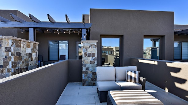 Eine Dachterrasse mit Steinmauer, einer Pergola mit Lichterketten, einer Couch und einem kleinen Tisch.