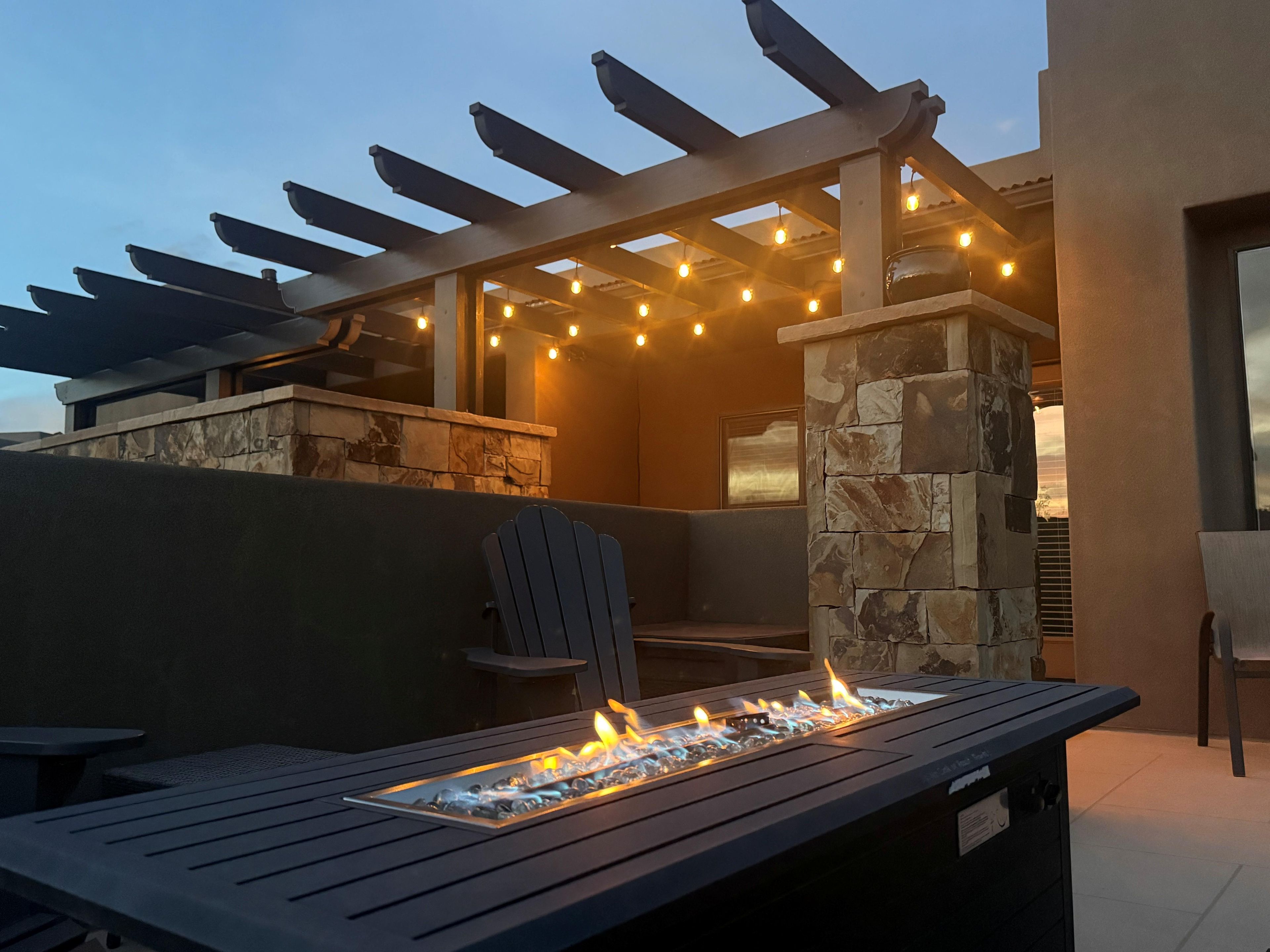An outdoor seating area with a fire feature, stone pillar, and string lights.